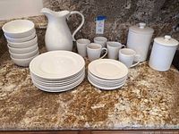 Full set of plates, bowls, mugs, pitcher and canisters displayed on countertop