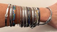 Stack of silver-tone and cloisonné bangles on wrist, showing variety of widths and patterns