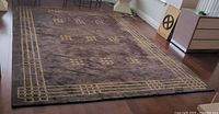 Full view of rectangular plum and gold geometric wool rug on hardwood floor