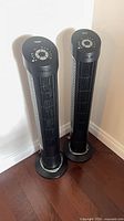 Pair of Seville Classics tower fans standing on hardwood floor