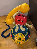 Full view of red M&M character telephone with yellow handset on base