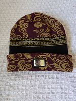 Front view of burgundy and gold beanie showing pattern, cuff, and Greek key band