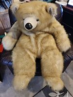 Full view of oversized tan teddy bear seated on chair