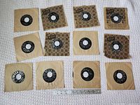 Twelve 45 RPM records arranged in three rows with sleeves and ruler for scale