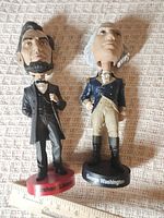 Both bobbleheads standing beside ruler