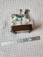 Side view of porcelain carousel horse on base with ruler for scale