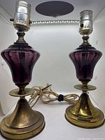 Front view of both brass and amethyst glass table lamps with cords visible