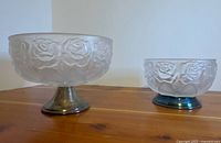 Large and small frosted glass rose pedestal bowls on wood surface