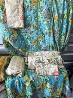 All three bedding groups arranged; blue floral coverlet draped, Thomason stripe set folded left, Tastemaster garden print set folded centre