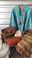 Group shot of two ponchos, backpack, scarves arranged on chair
