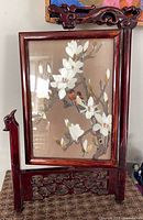 Front view of silk embroidery in carved wood stand