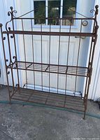 Front view of wrought iron rack showing three shelves and scroll accents