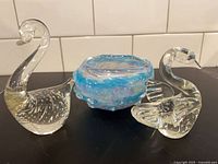 Blue swirl art glass bowl flanked by two clear glass swan figurines