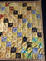 Full section of yellow and multicolour patchwork quilt with tan binding