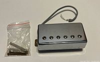 front view of chrome humbucker with bag of screws and springs