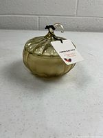 Front view of closed yellow glass pumpkin candle jar with tag attached