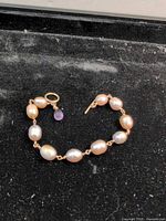 Full view of pearl bracelet laid flat showing clasp and amethyst charm