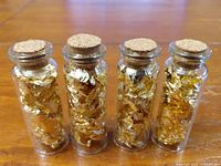 Front view of four cork-topped glass vials filled with gold leaf flakes