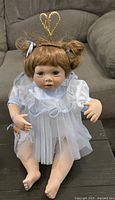 Front view of porcelain baby angel doll seated, showing dress, halo, hair ribbons and limbs
