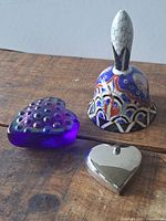 Multicolour ceramic bell, purple glass heart paperweight, silver-tone heart box on wooden surface