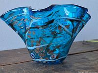 Front angled view showing ruffled shape, blue color, internal canes and flecks