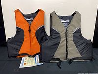 Front view of both Stearns life jackets, orange-black and tan-black