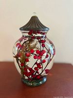 Front view of glass oil candle displaying red berries, fern and lid