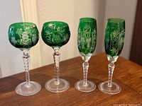 Front view of four Ajka emerald green cut-to-clear stemware pieces on wood surface