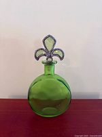 Front view of emerald green glass decanter with fleur-de-lis stopper