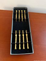 Overall view of eight gold-tone bamboo-style cocktail forks in box