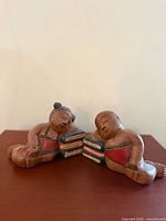 Full view of both carved wooden bookends leaning on stacks of books