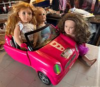 Front view of three 18" dolls positioned around pink American Girl convertible car