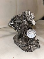 Full view of metal dragon statue with faceted orb on base