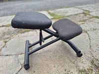 Side view of black ergonomic kneeling chair showing seat, knee pad, and steel frame