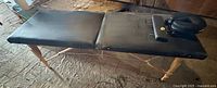 Full view of unfolded black foldable massage table on wooden legs