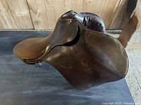 Right side view of brown leather saddle showing seat, cantle and flap