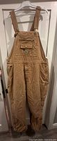 Front view of brown Carhartt duck bib overalls hanging on hanger