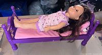 Doll lying on purple doll bed, side view