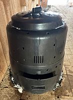 Full front view of black Earth Machine compost bin showing vent holes and lower access panel
