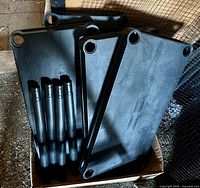 Box containing four black plastic shelf panels and five black plastic support posts