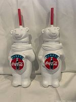 Front view of two white plastic Coca-Cola polar bear bottles with red straws