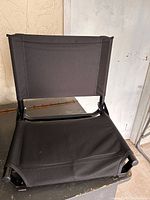 Front view of folded black stadium seat showing padded canvas seat and backrest