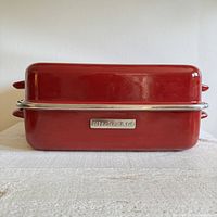 Side view of closed red KitchenAid roasting pan showing brand badge and chrome rim