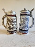 Front view of both steins showing relief scenes and lids