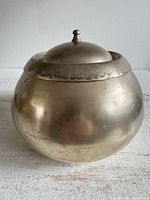 Front view of rounded metal chamber pot with lid in place showing overall form and finish