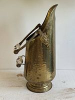 Front angled view of hammered brass coal scuttle showing Delft handle and lion head mount