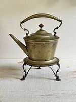 Front left view of kettle on stand showing spout, handle, ornamentation