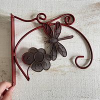 Front view of red painted metal bracket showing dragonfly and flower design