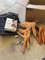 Lot overview showing boxed Magic Bag, stack of black garment covers, pile of wooden coat and pant hangers