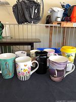 Front view of eight ceramic mugs displaying various designs